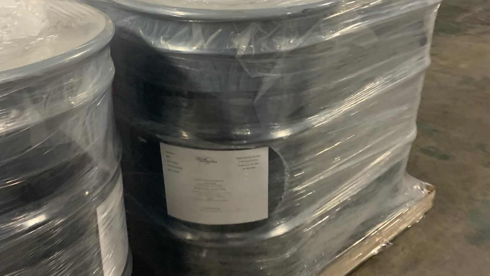 Four black 55-gallon Cattie Adhesives drums stretch-wrapped on a pallet