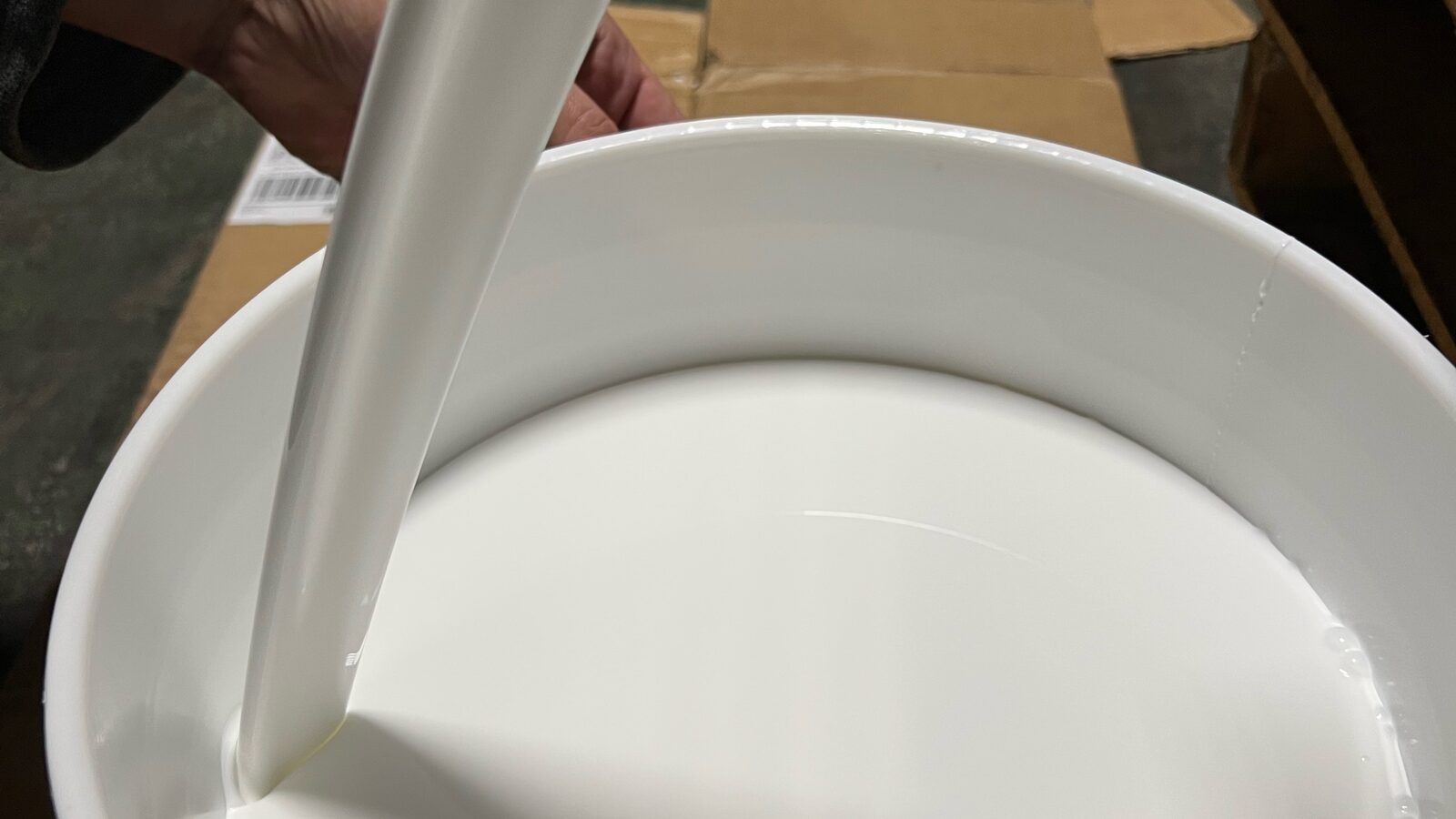 White water-based adhesive pouring into a pail in the Cattie plant