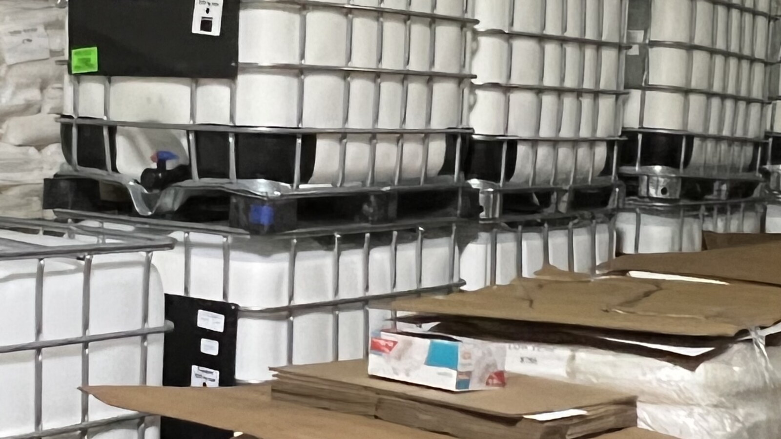 Cattie Adhesives warehouse aisle with cartons, IBC totes, and bagged product